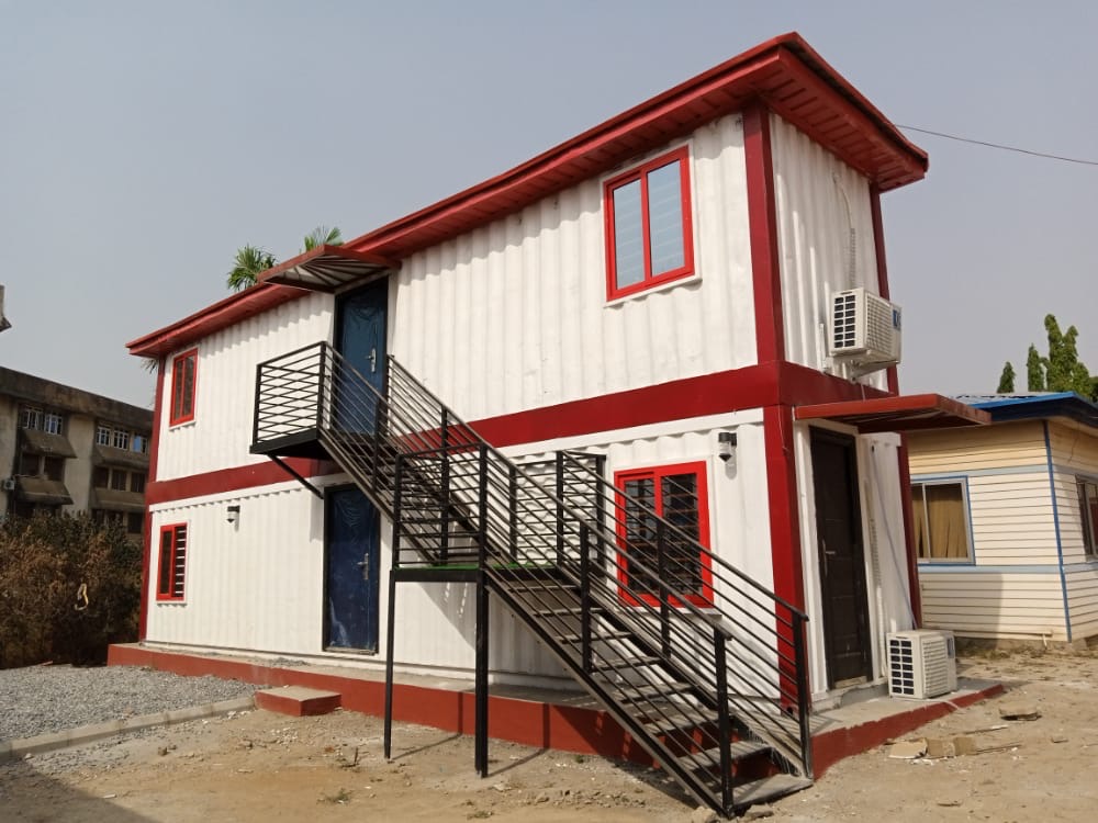 Two-storey container house with red trim and an external steel stair